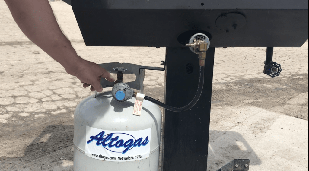 Hand connecting a propane tank to a grill with an Altogas label.